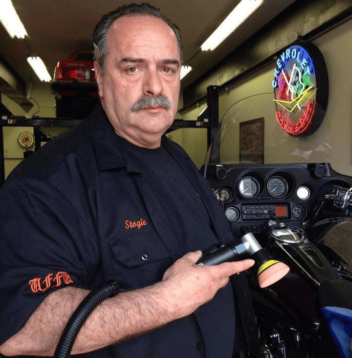 Harry Sandwith holding a polisher beside a motorcycle in his shop